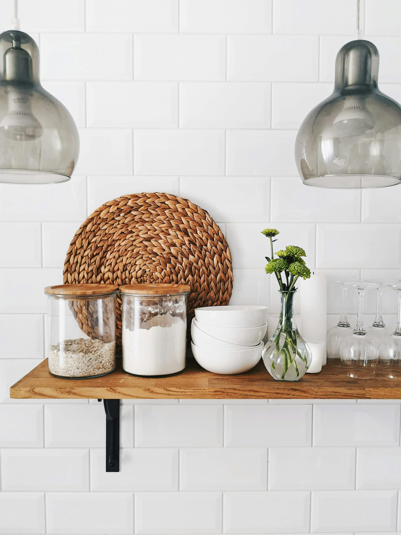 Open kitchen shelf with glass storage jars, bowls and a woven mat
